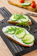 Healthy breakfast or snack: Cucumber, cream cheese and arugula toast on wooden cutting board