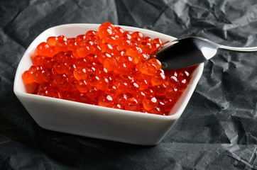 spoon in salmon caviar in a white bowl horizontal on a black bac