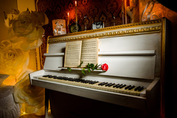red rose on piano keys and music book