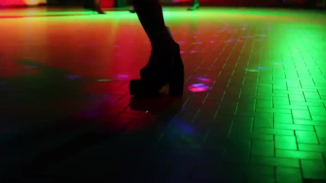 woman in boots dancing on defocused floor of a disco club with high changing strobe  lights of blue, red and pink