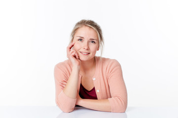 serene smile - calm young blond woman sitting in a sparse office smiling to express her wellbeing, white background studio