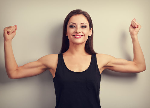 Pleased strong fit woman showing muscle biceps with happy smilin