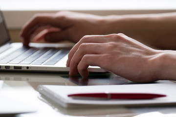 hands of a young man typing on laptop computer with notepad and pen on glass deck