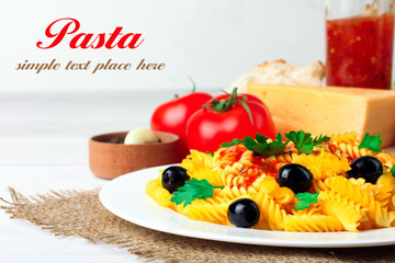 fusilli pasta and olives in the dish by the fresh tomatoes and peppers with garlic and cheese lying on a wooden white background with space for your lettering