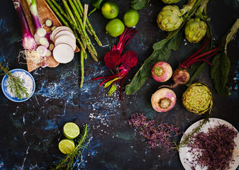 Still life of green fruits and vegetables roots over dark marble table.