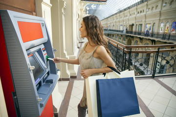 Young happy brunette woman withdrawing money from credit card at