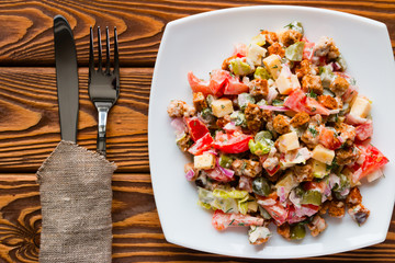 vegetable salad with mayonnaise in white plate next to the cutlery on a napkin