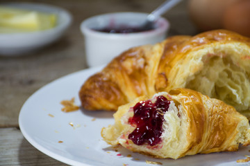 fresh croissant with red fruit jam for breakfast on a rustic wood