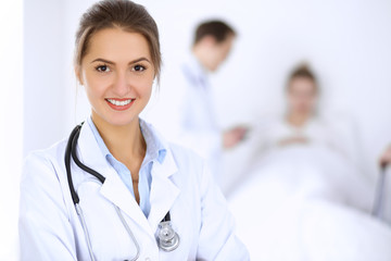 Fototapeta premium Female doctor smiling on the background with patient in the bed and two doctors
