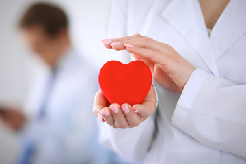 Femail doctor holding a red heart in his hands on a background of the patient. Health care concept