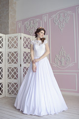 Beauty bride in bridal gown indoors. Beautiful model girl in a white wedding dress. Female portrait of cute lady. Woman with hairstyle
