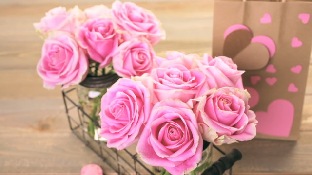 Pink roses in jars on rustic wood table.