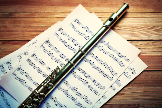 Flute on musical notes and on wooden table background