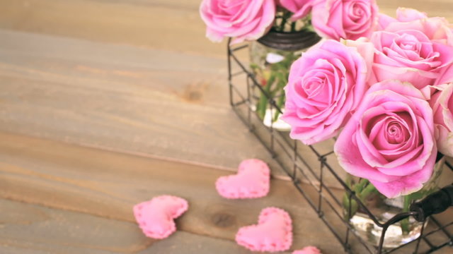 Pink roses in jars on rustic wood table
