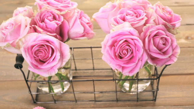 Pink roses in jars on rustic wood table

