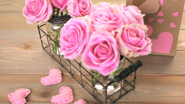 Pink roses in jars on rustic wood table.
