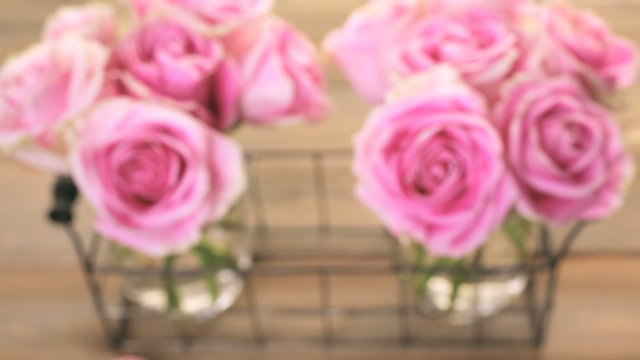 Pink roses in jars on rustic wood table.
