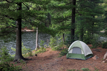 A green tent setup right beside a lake.  Shot in Algonquin Provincial Park, Ontario, Canada..