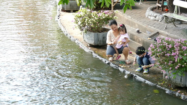 Asian mother and her children feeding food for fish in pond