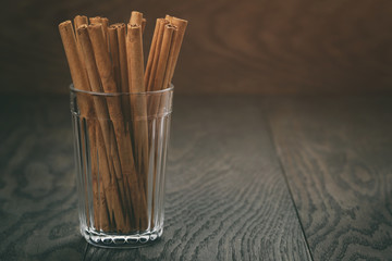 true cinnamon sticks in glass on wooden table, vintage toned photo