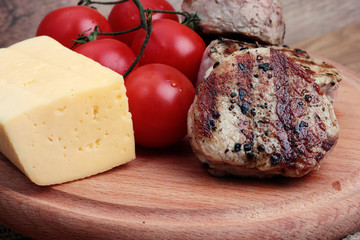macro grilled meat with tomato on wooden plate with cheese and herbs , pepper
