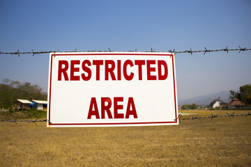 Restricted area sign, red words on white background, barbed wire