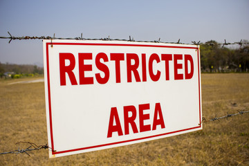 Fototapeta premium Restricted area sign, red words on white background and barbed wire
