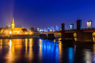 Illuminated bridge across Nemunas river and old town cityscape at night, Kaunas, Lithuania.