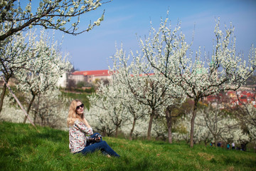 girl with camera is sitting in the garden of blooming apple trees