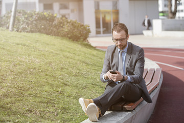 Fototapeta premium Businessman using his smart phone while resting on the bench 