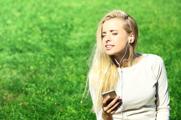 Naklejka premium Young woman with earphones and smartphone listening to music on grass