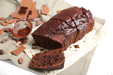 Chocolate sliced cake with icing and cocoa powder on tablecloth