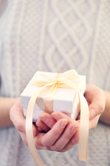 Female hands holding beautiful small gift wrapped with satin ribbon.