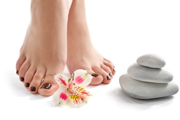 Obraz na płótnie Canvas Manicured female feet with spa stones and flowers isolated on white