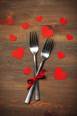 Fork and knife with decorative paper hearts, on wooden background
