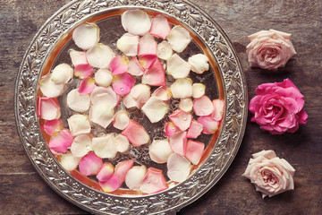 Pink and white rose petals in silver bowl on wooden background