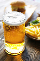 Glass mug of light beer with French fries on dark wooden table, close up