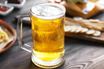 Glass mug of light beer with snacks on dark wooden table, close up