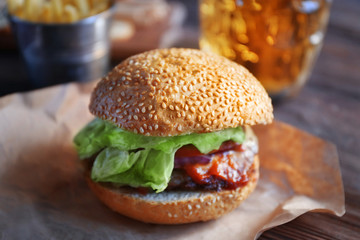Big tasty hamburger on a paper with light beer in glass mug, close up
