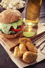 Big tasty hamburger with snacks and glass bottle of light beer on wooden table