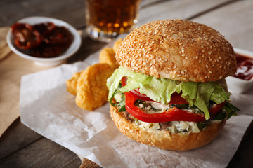Big tasty hamburger with snacks and glass mug of light beer on wooden table