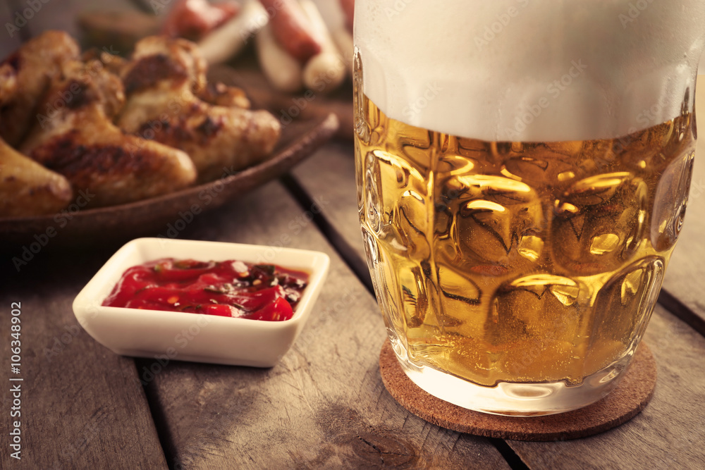 Wall mural Glass of beer, chicken wings and grilled sausages on wooden table, close up