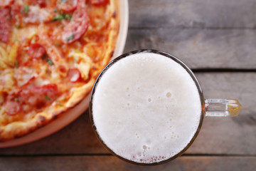 Tasty pizza and glass of beer are on wooden table, close up