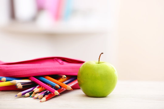 Apple and pencil-box full of pencils on table in the room
