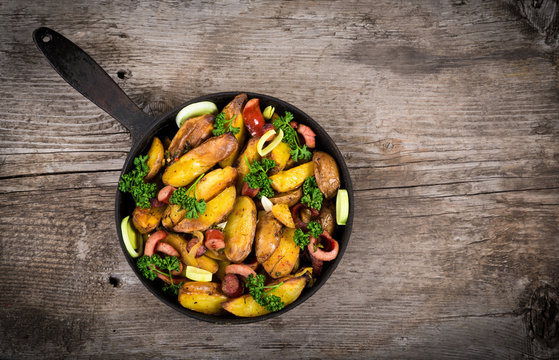 Fried potatoes with sausages on wooden table