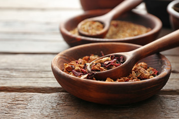 Variety of tea in round bowls with spoon on wooden table, close up
