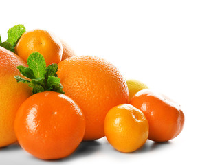 A heap of mixed citrus fruit including a grapefruit, oranges, lemons, clementines, tangerines with mint sprigs isolated on a white background, close up