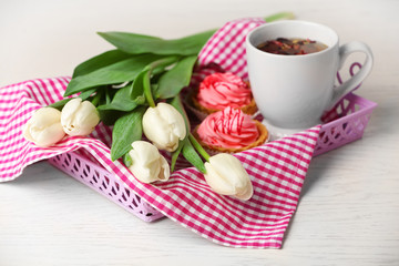 Still life with fresh bouquet of tulips, cupcakes and cup of tea on wooden table closeup