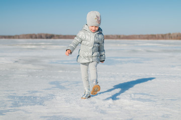 Fototapeta na wymiar Радостный ребенок бежит по замерзшему озеру в солнечный день ранней весной