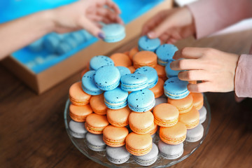 Female hands taking tasty macaroons from dish on the table